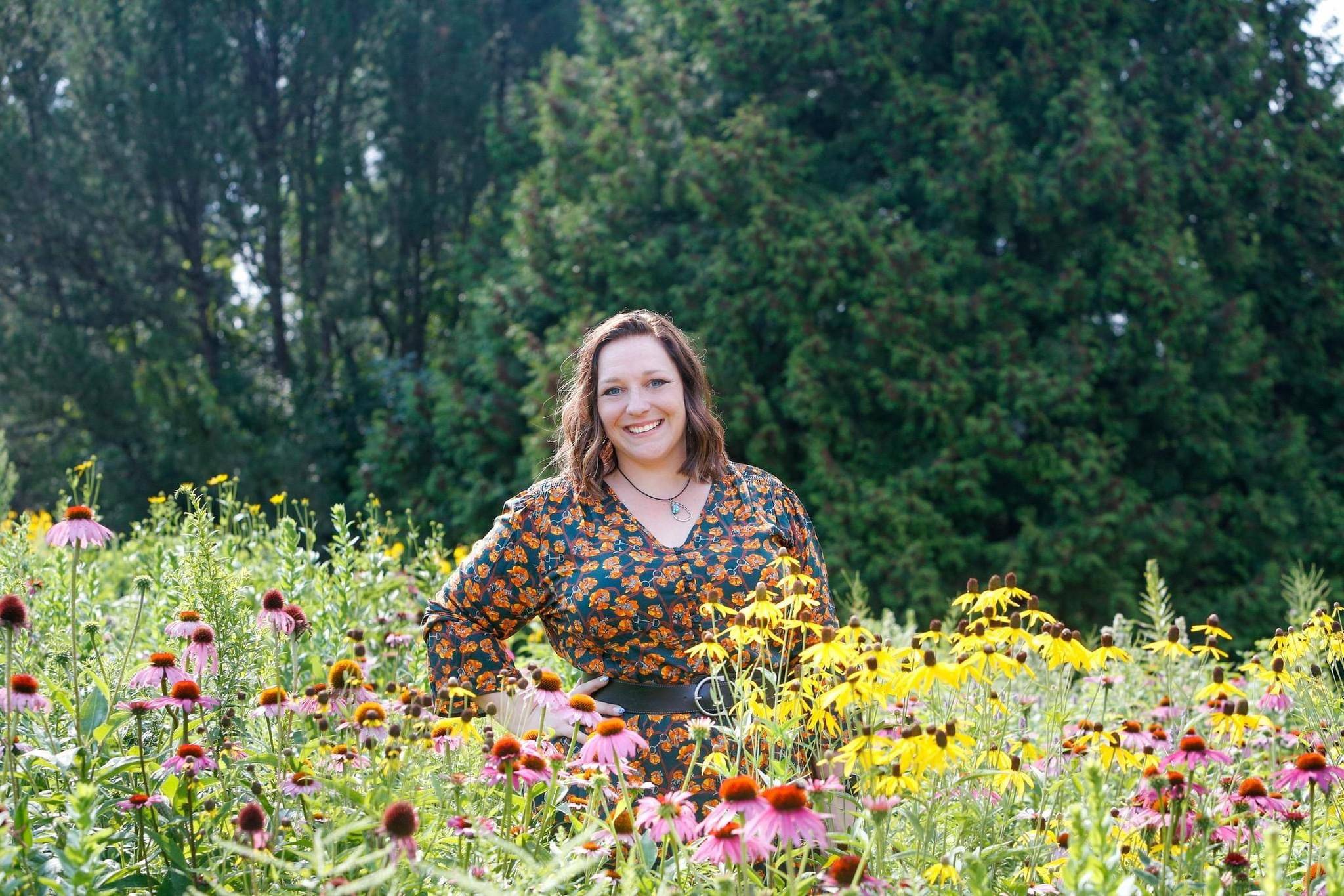 Photo of Janet Cram, owner of Two Cents Accounting, standing in a field of wildflowers with pine trees in the background