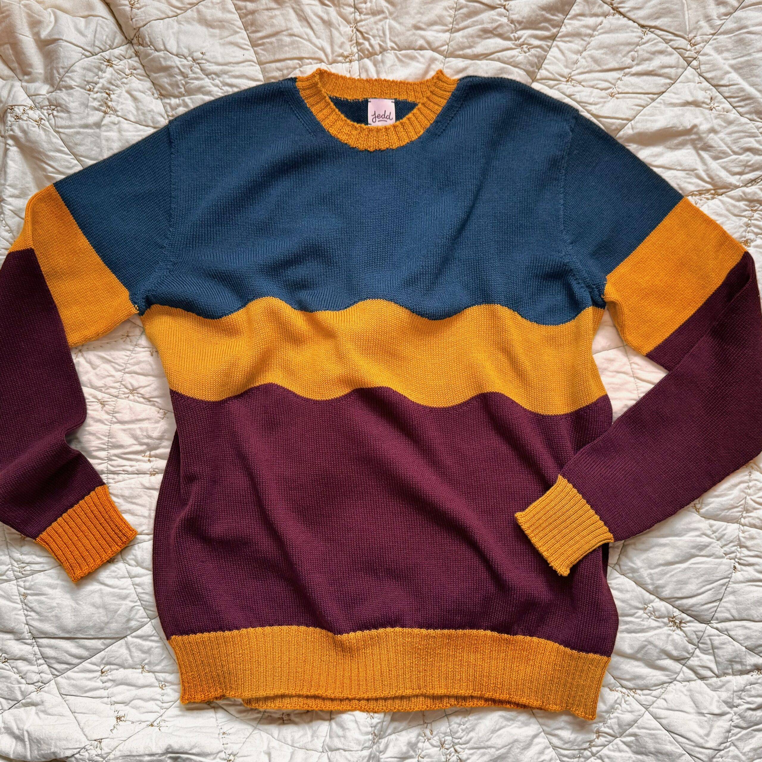 A merino sweater with a blue top, yellow stripe, and maroon bottom