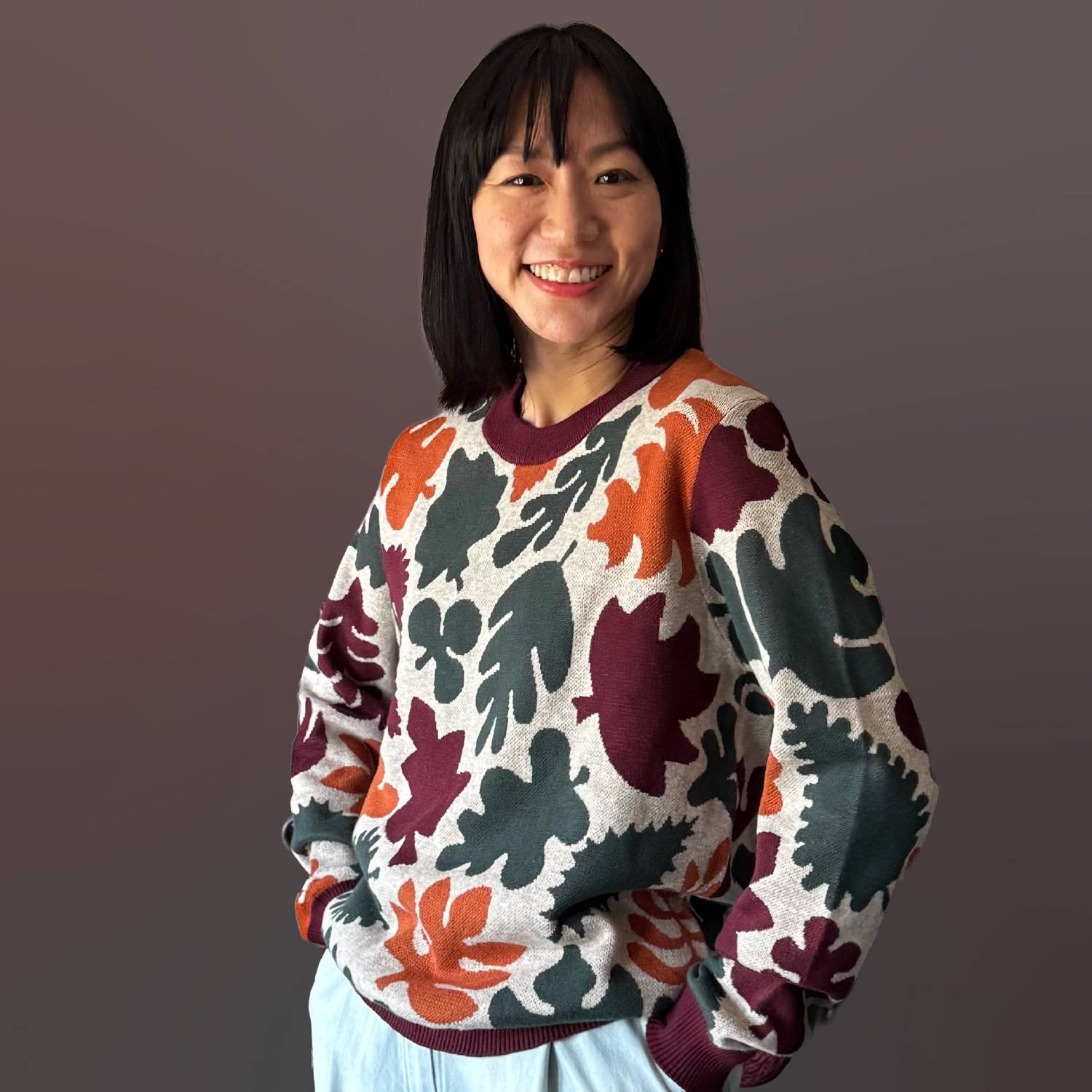 A woman wearing a tan sweater with detailed leaf patterns