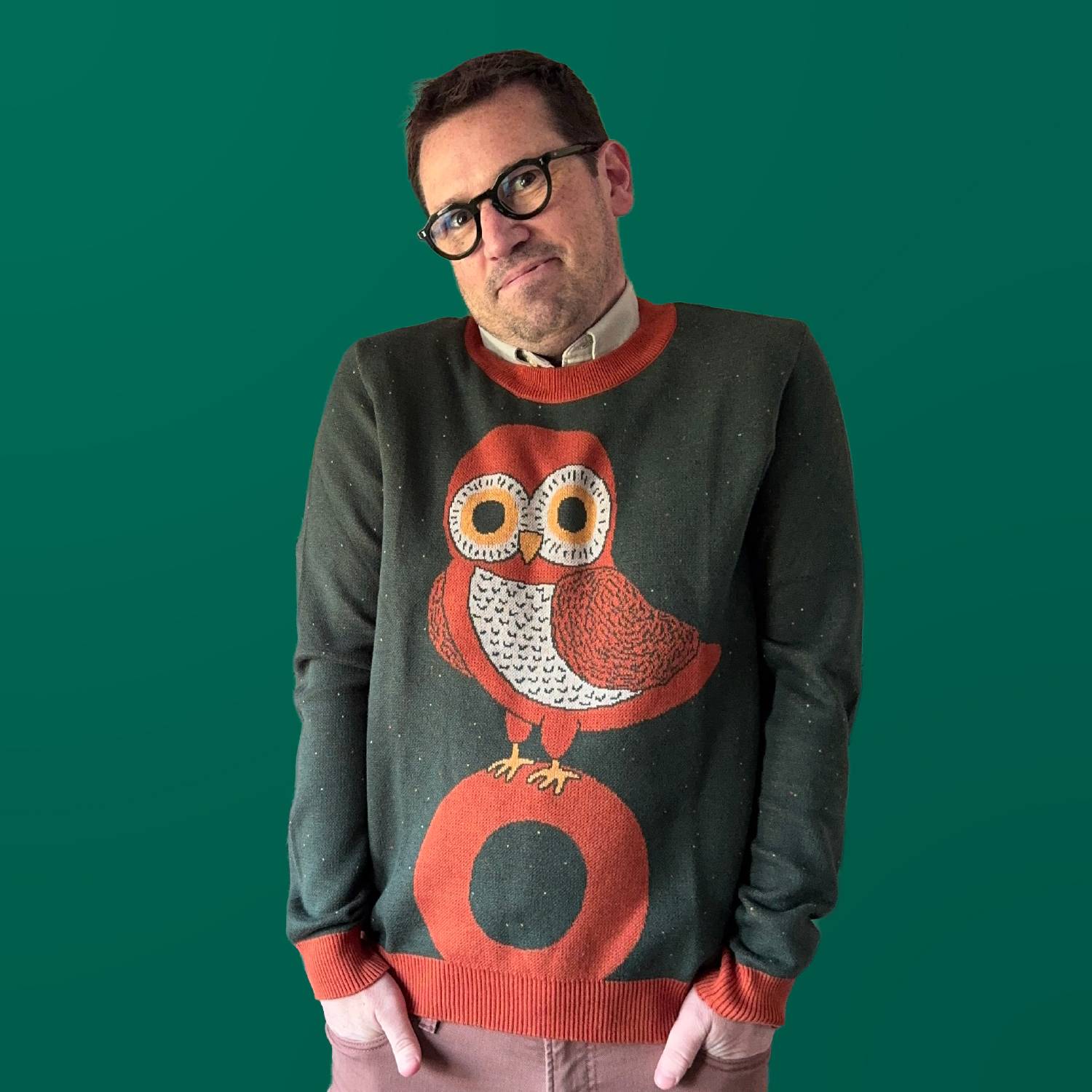 A portrait of Jedd wearing a green sweater with an owl design.