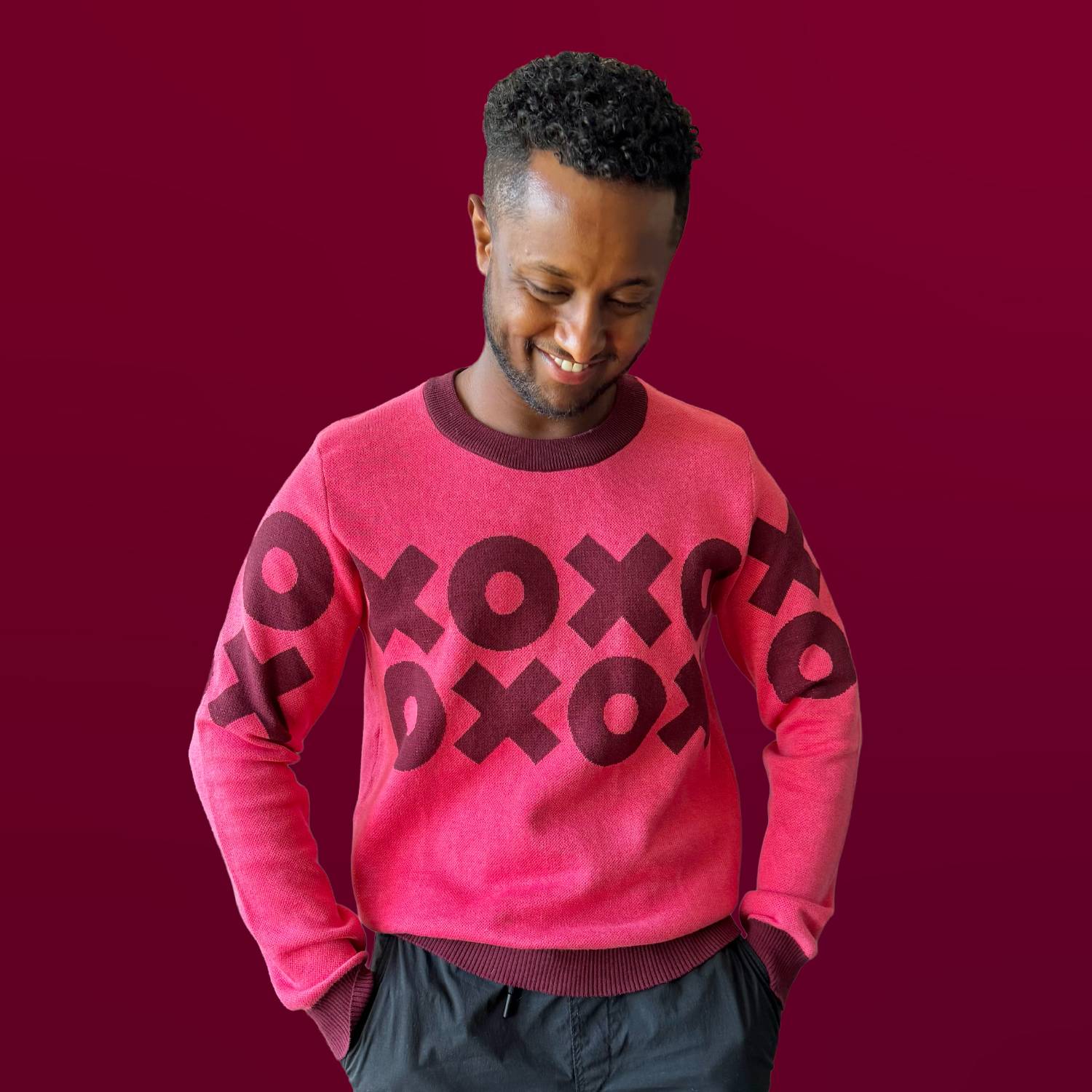 A man wearing a pink sweater with an XOXO design across the garment.
