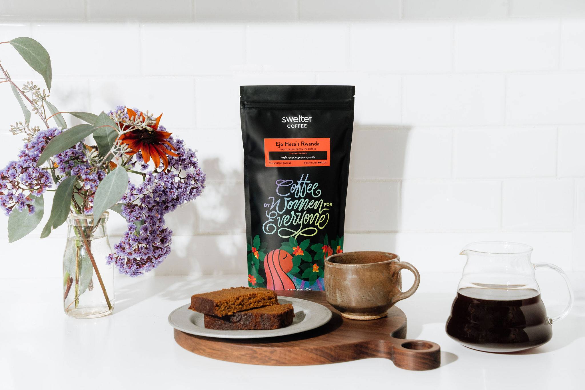 Bag of coffee on a white countertop with a mug and pastry in front