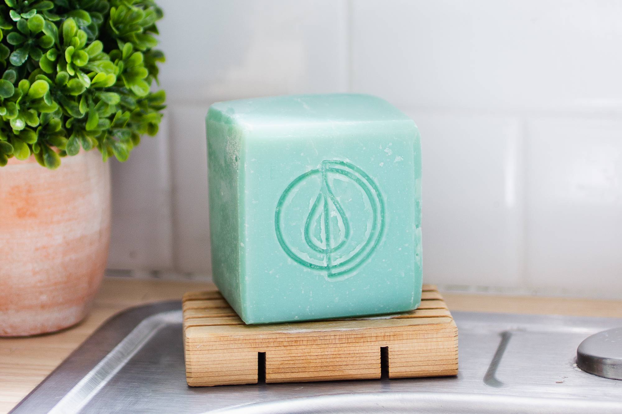 light blue bar of solid dish soap on a wooden soap dish on the side of a kitchen sink