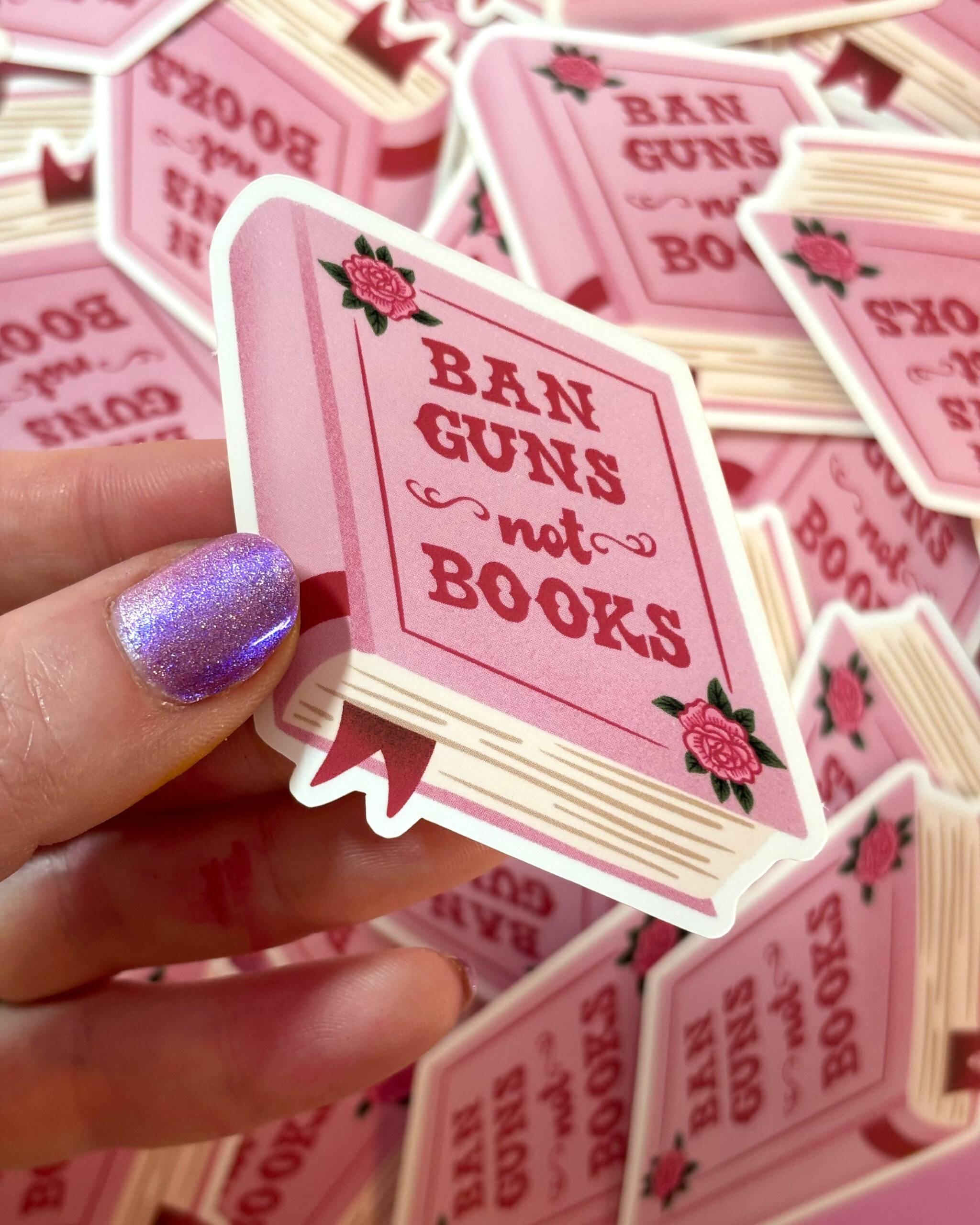 A hand holding a pink vinyl sticker of a book with text 