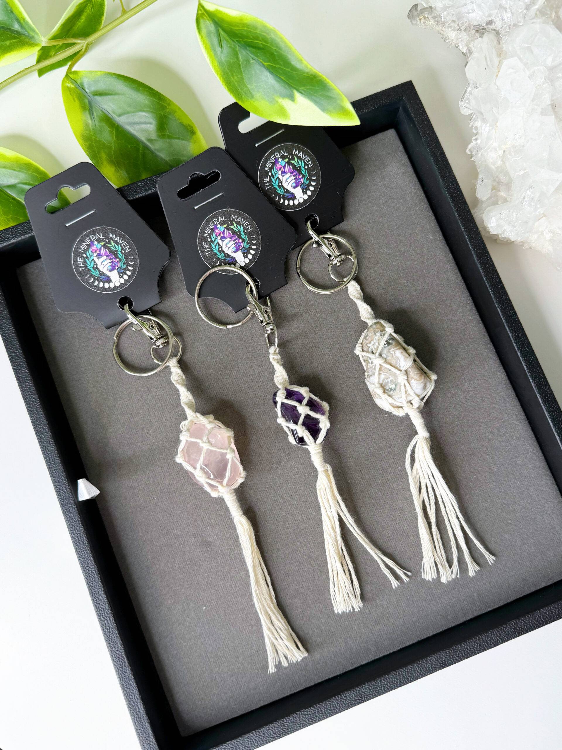 Macrame keychain tassels containing a tumbled stone within the netting, 3 of these on a black tray.