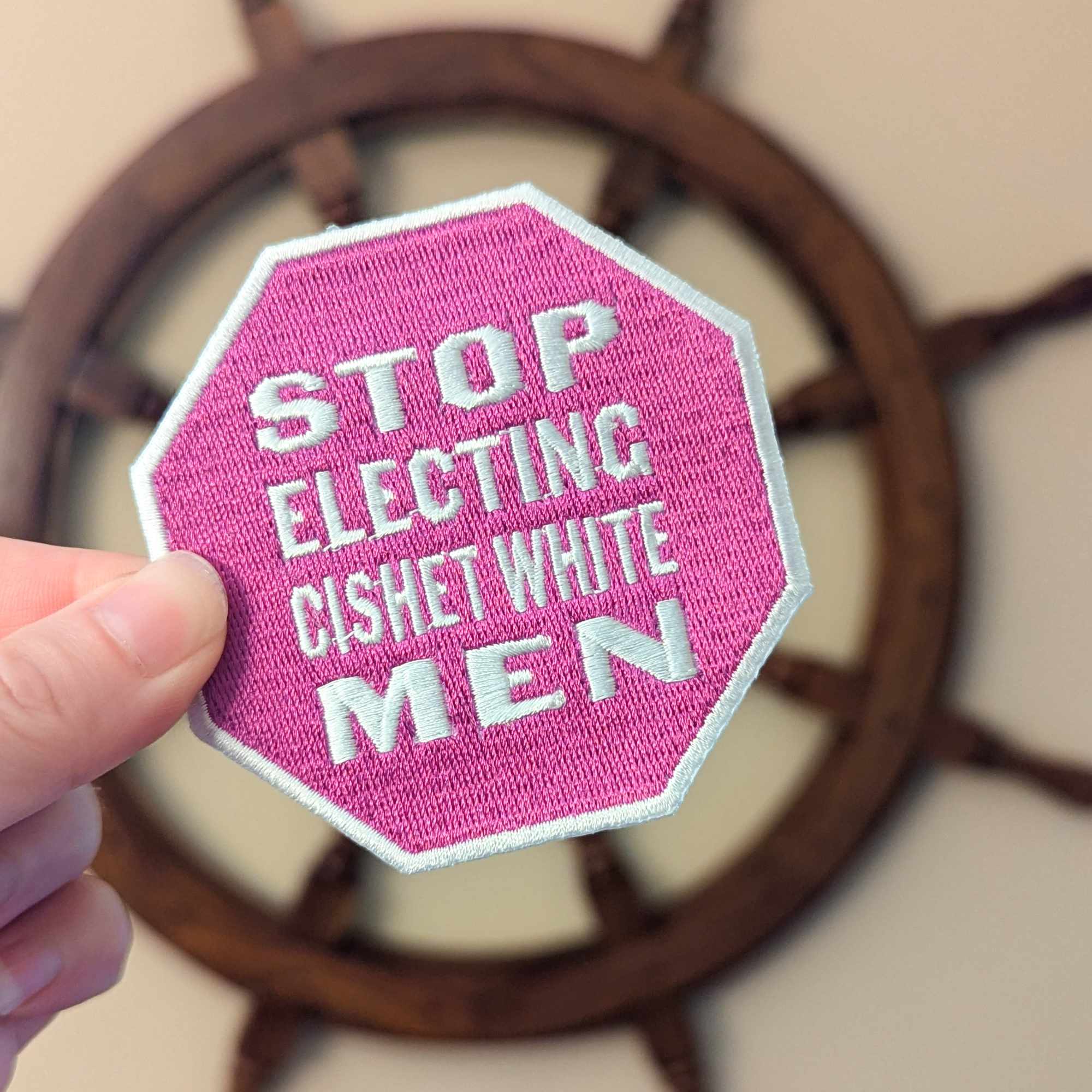 A pink embroidered patch in the shape of a stop sign; white text reads 
