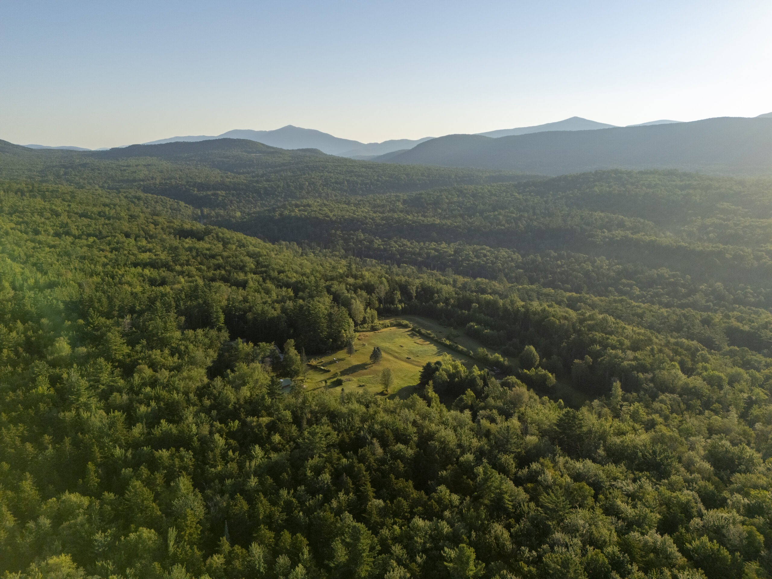 Drone photo of the property showing the meadow surrounded exclusively by trees and mountain peaks.