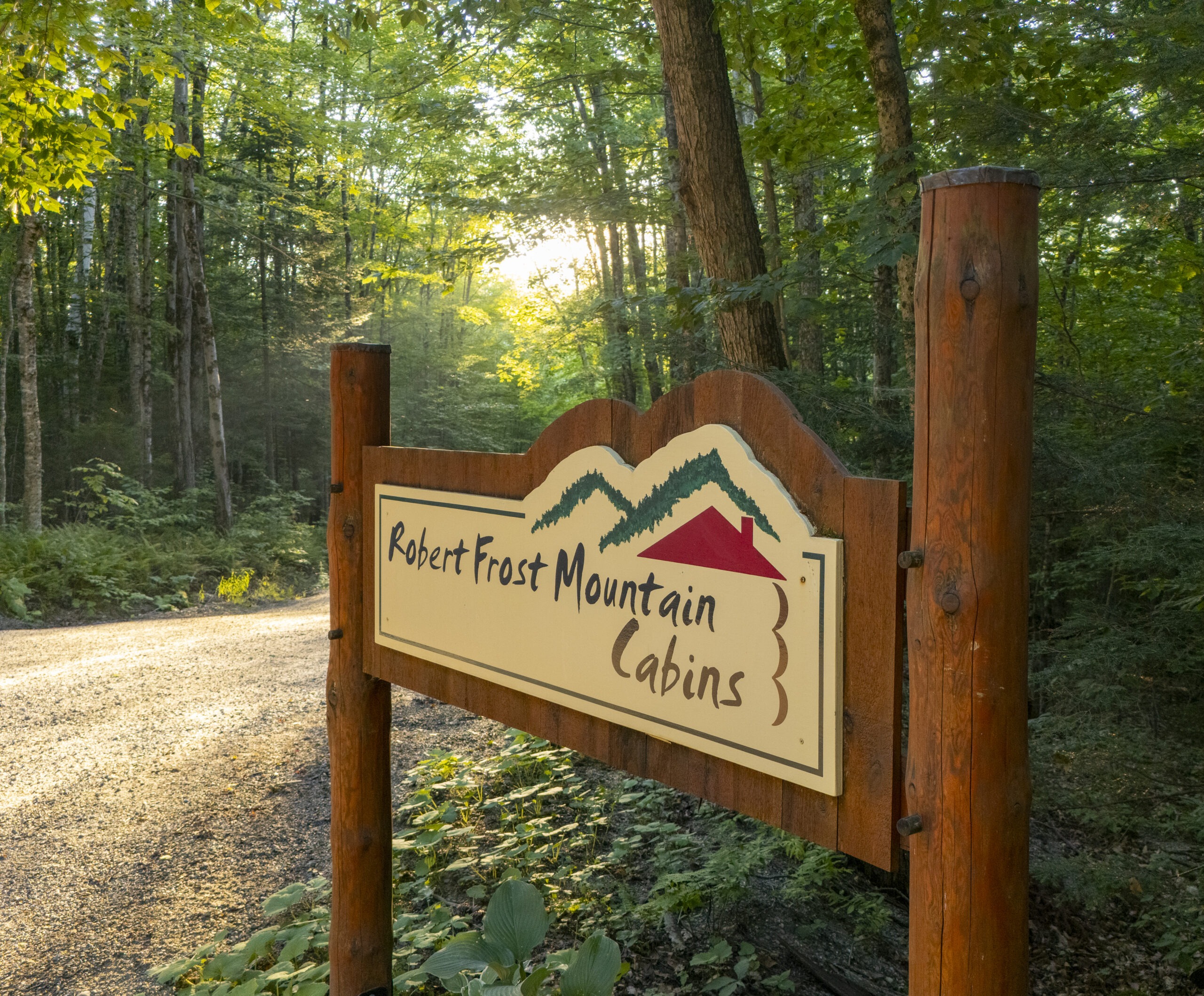 Top drive way sign depicting the Robert Frost Mountain Cabins name underneath two artistically rendered mountain peaks and the outline of a cabin.