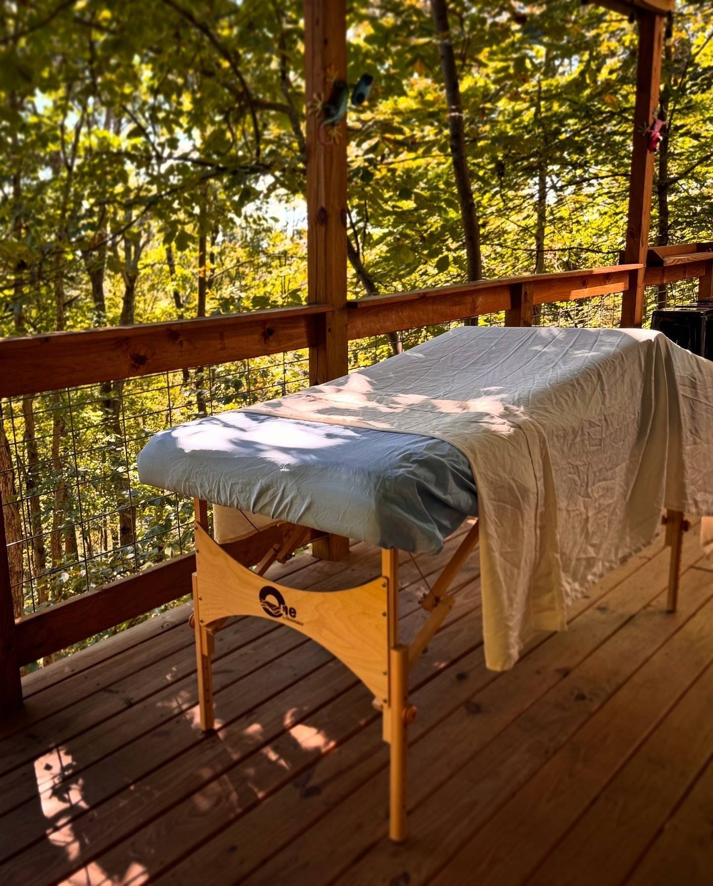 Massage table set up on porch, surrounded by trees that are starting to show their fall colors