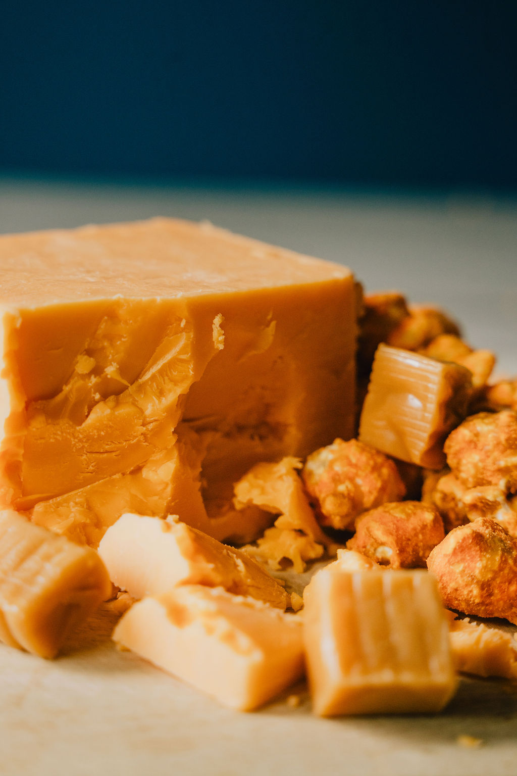 Chunk of cheddar cheese with caramel cubes and caramel cheddar popcorn laying with it
