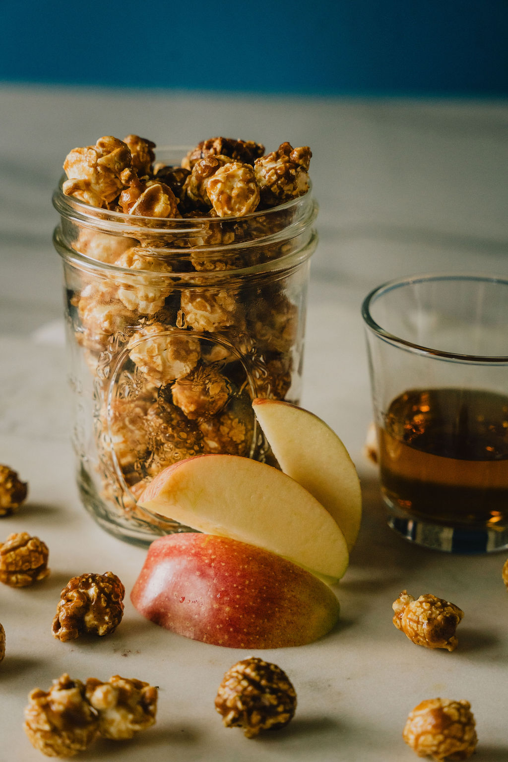 Spiked Apple Butter Caramel Corn with sliced apples and a glass of moonshine