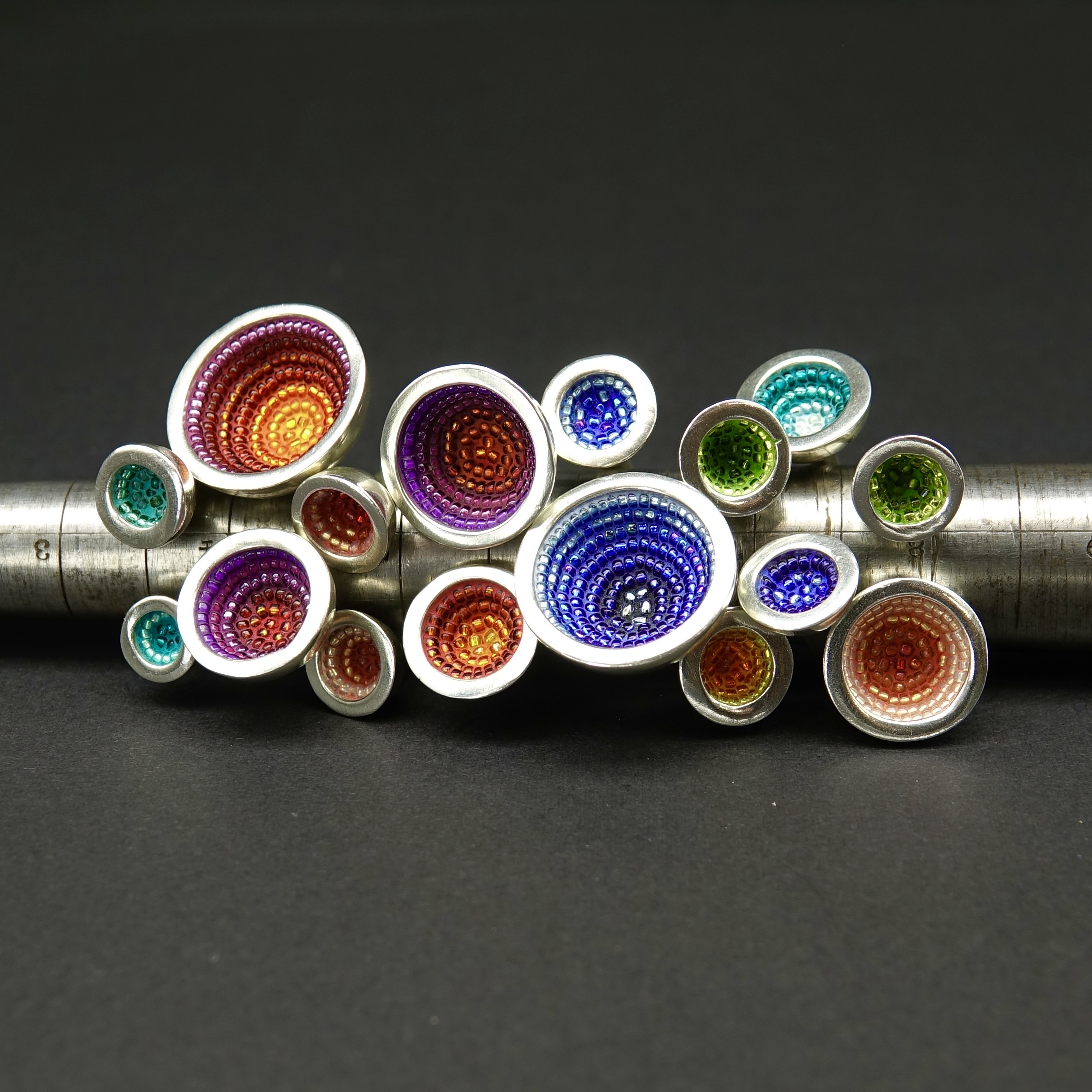 A stack of colorful bowl-shaped rings on a graduated steel ring mandrel