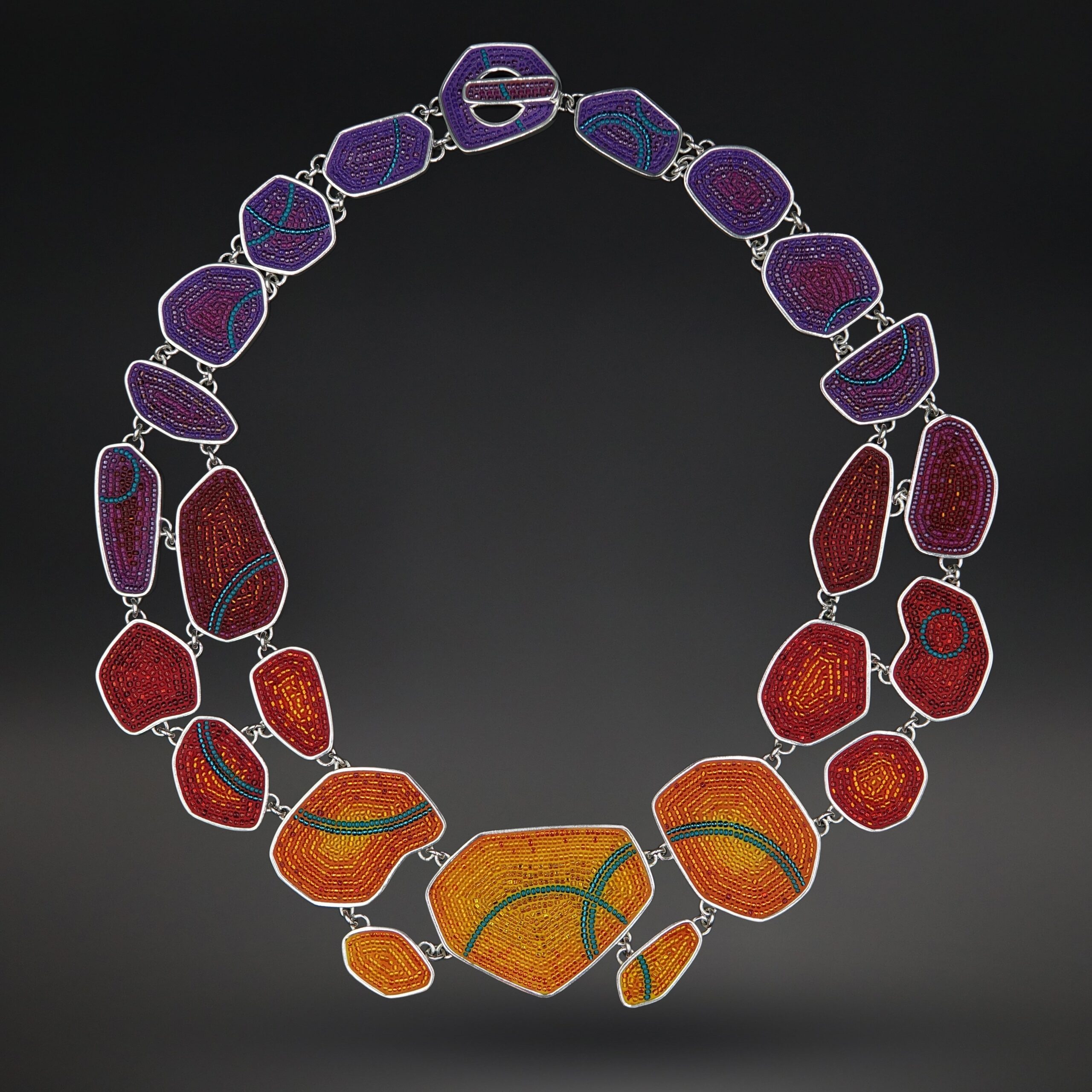 A necklace of 24 differently shaped, graduated pebbles of sterling silver inlaid in colorful beaded micro-mosaics. Subset colors ombre effect from purples in the back to raspberry reds and then golden orange hues in the center.