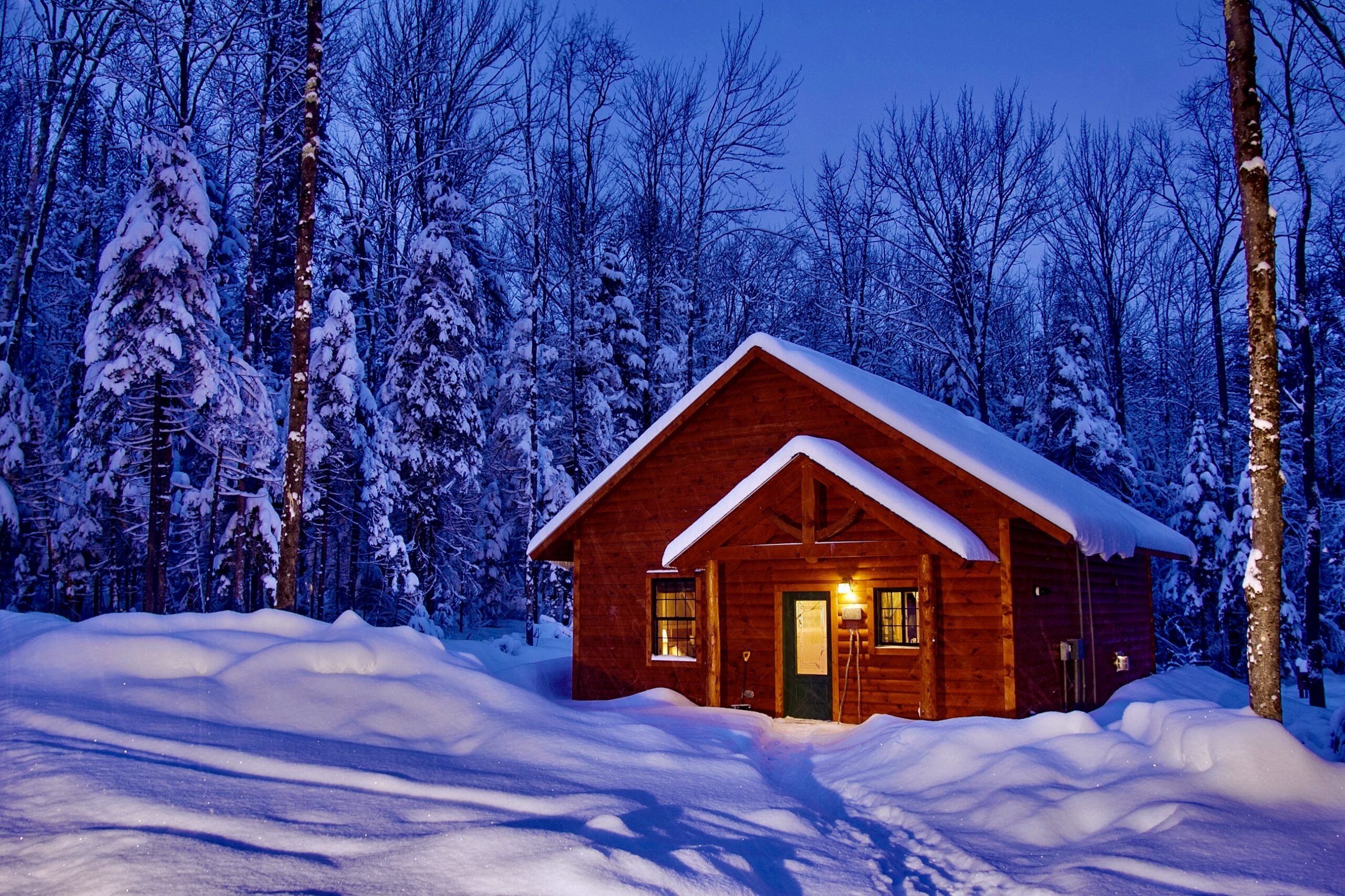 Cabin 6 in the snow at dusk. The warm lights from the front door and windows create a warm, inviting vibe.