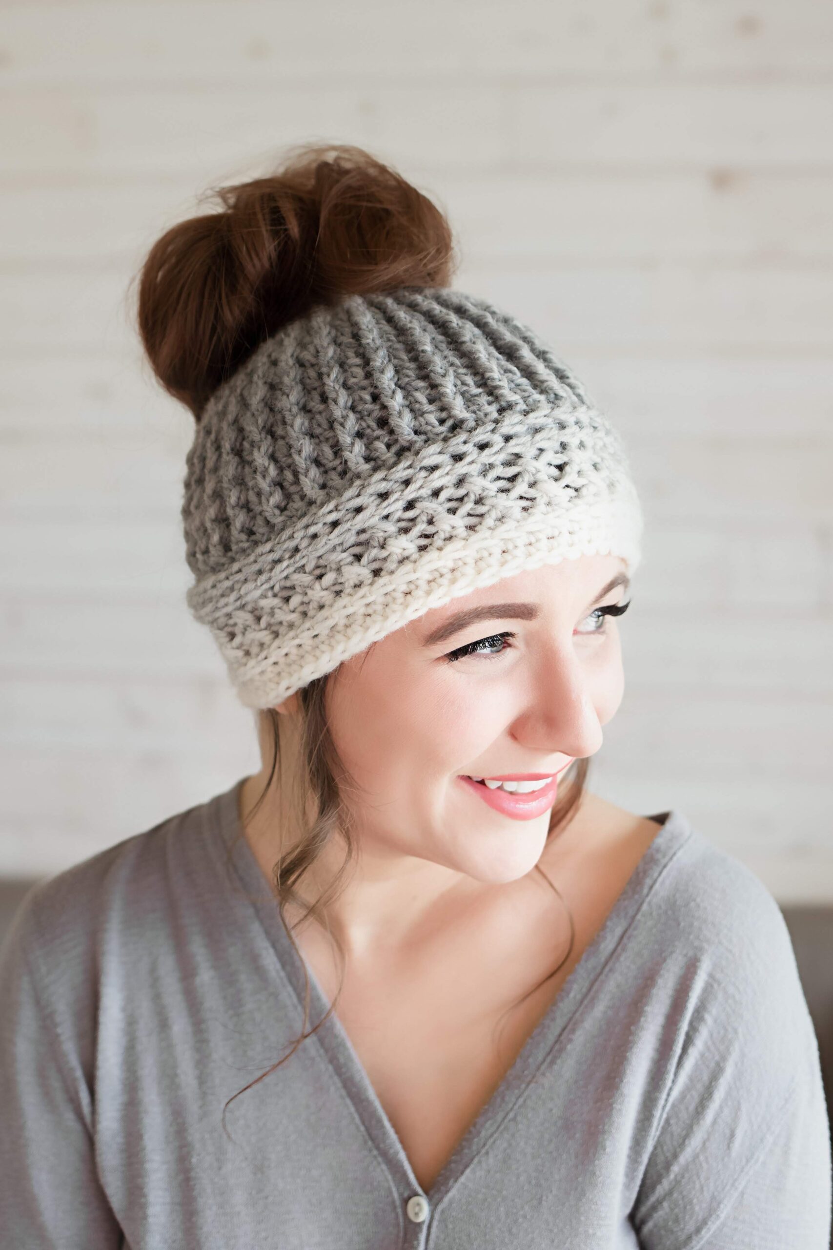 A woman wearing a cream and grey ombre hat, with her bun poking out the top of the hat