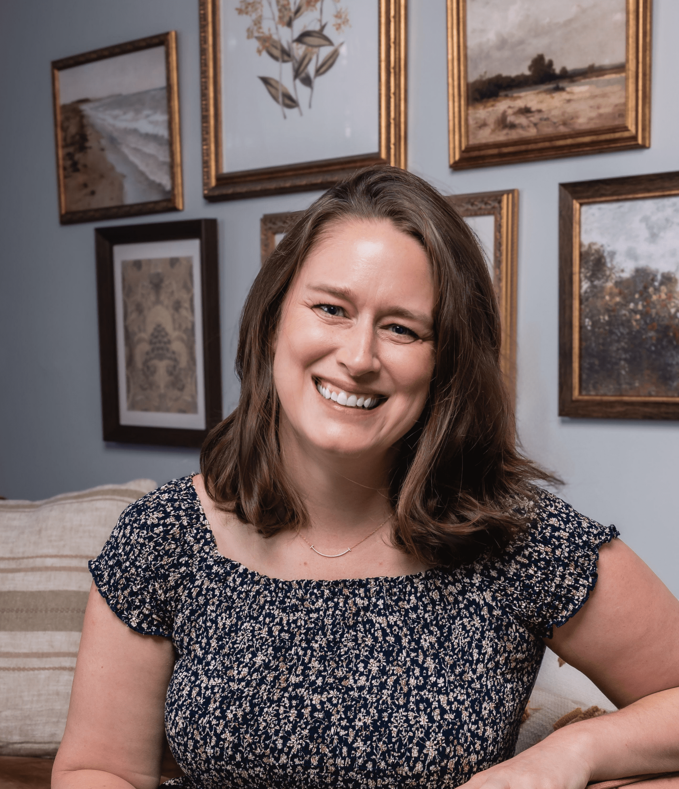 Lauren Strine, LMFT in Atlanta, perinatal mental health therapist, wearing blue floral top with gallery wall behind her.