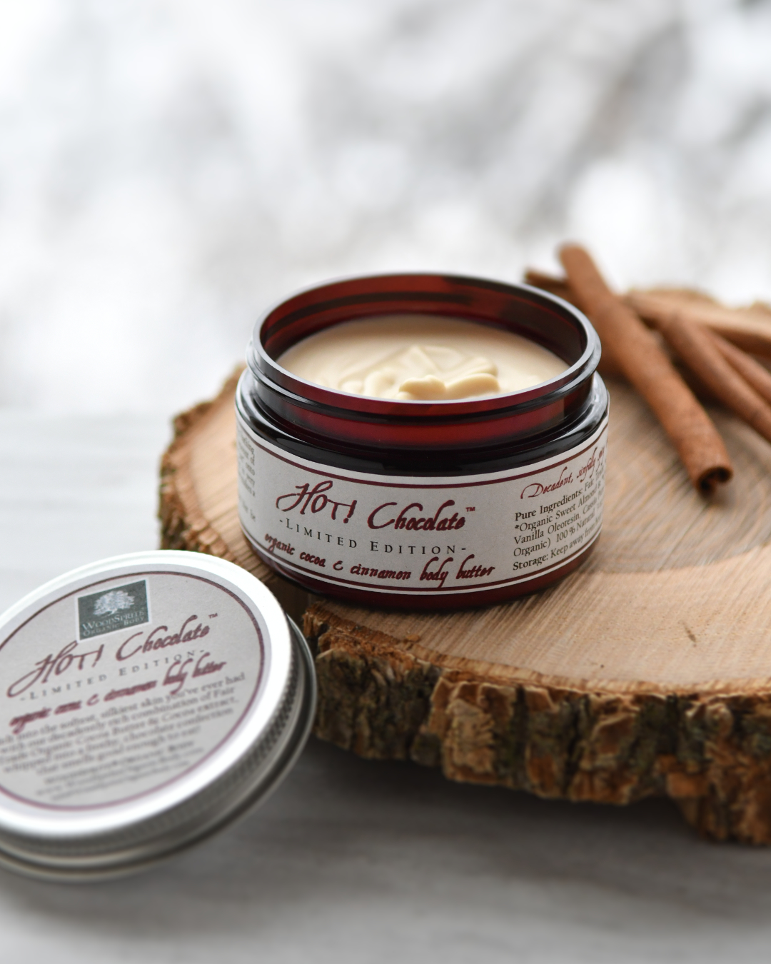 Hot Chocolate Organic Whipped Body Butter jar on a wood charger and a snowy scene.
