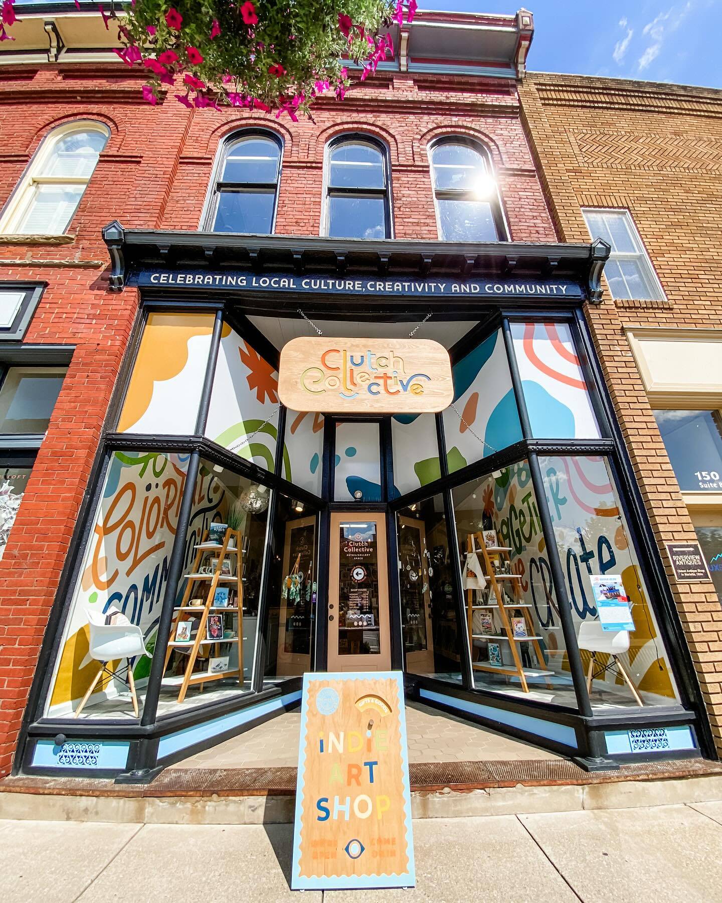 A bright and colorful facade of an art shop with a hand-painted sandwich board in front
