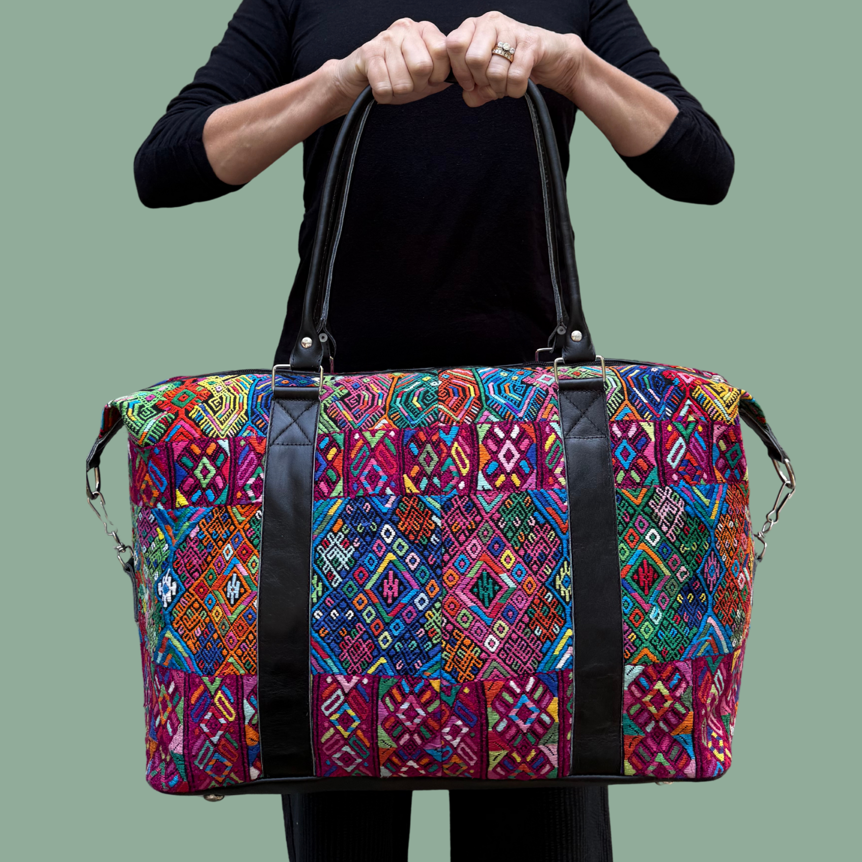 Colorful handwoven travel bag, trimmed in leather, and held for display by a woman in black clothing