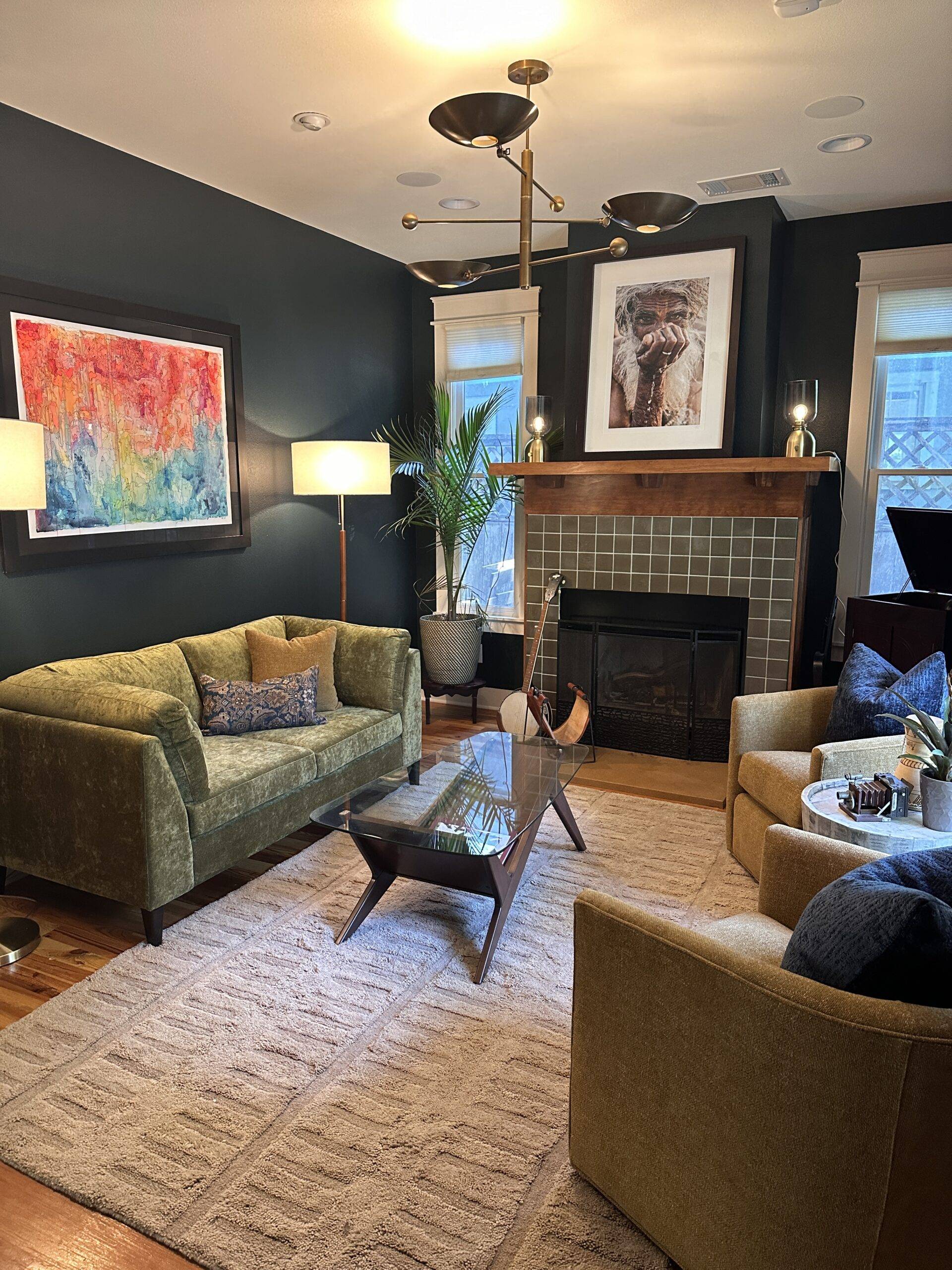 Moody blue parlor room with bright green leather sofa and large photograph of man above tiled fireplace.