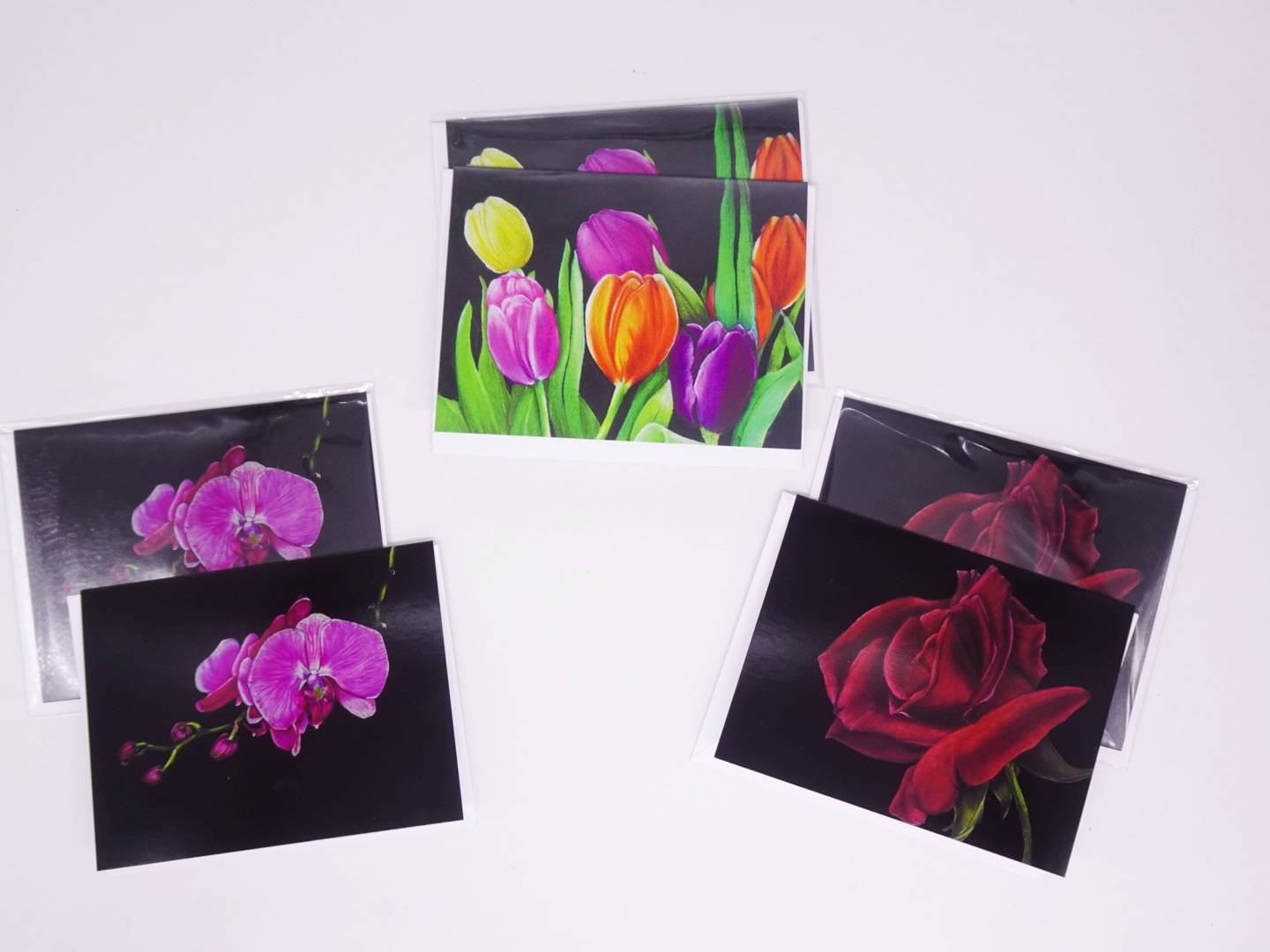 Floral greeting cards arranging in an arc. Left to right, purple orchid, multicolored tulips, red rose. All are on black backgrounds.
