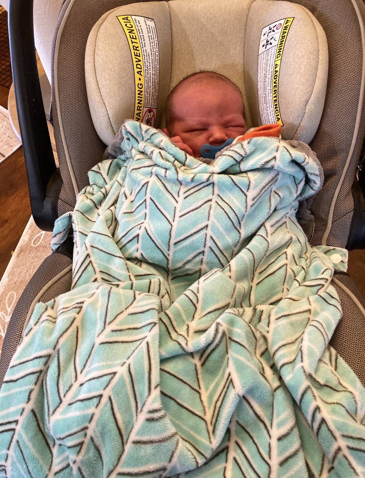 A newborn strapped into their car seat, with a Cocoona slid on and covering their body to keep them warm.
