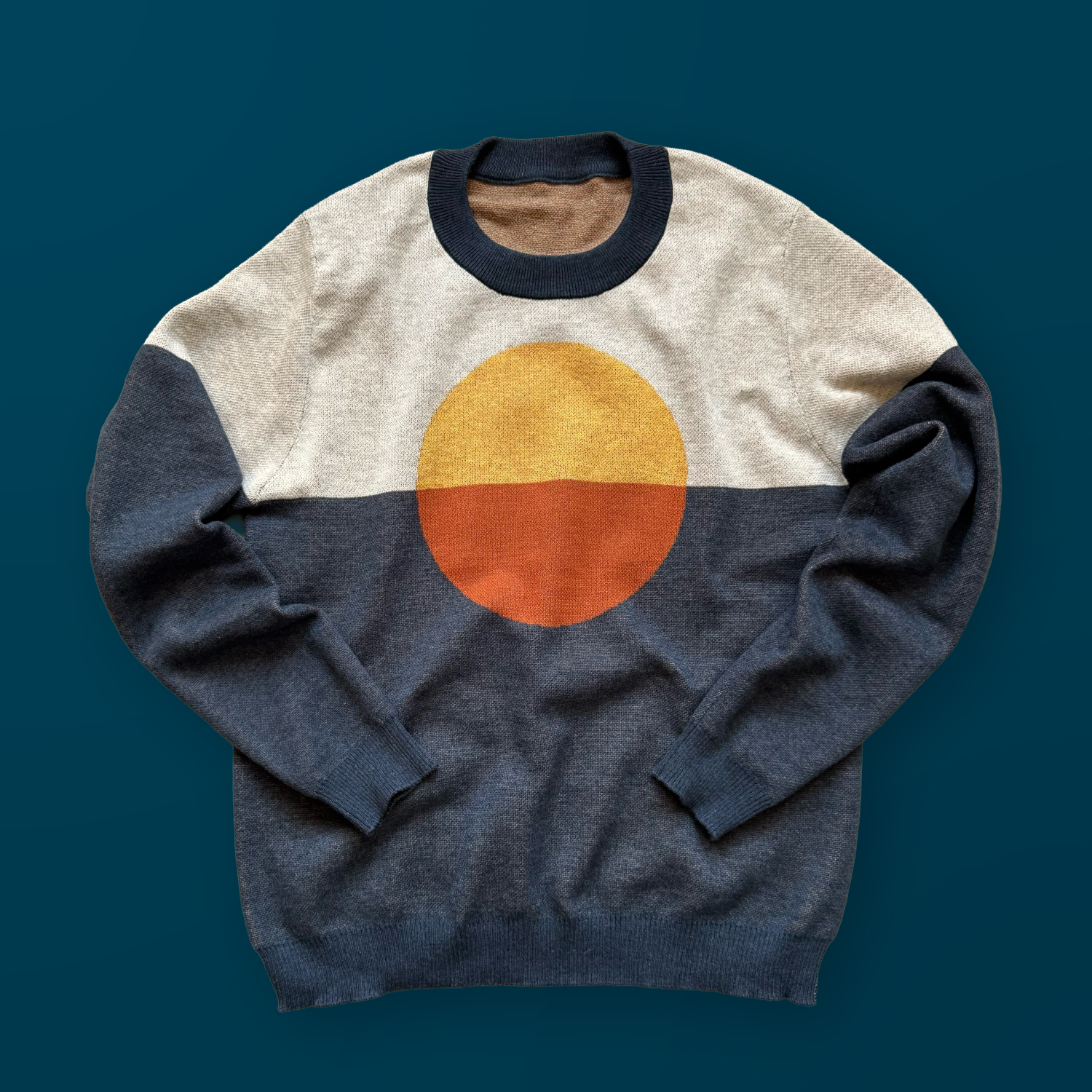 A blue and gray sweater with a orange and yellow circle design in the center