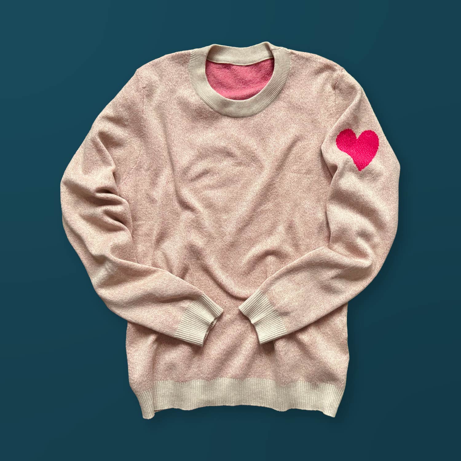 A cream colored sweater with a red heart design on the left sleeve
