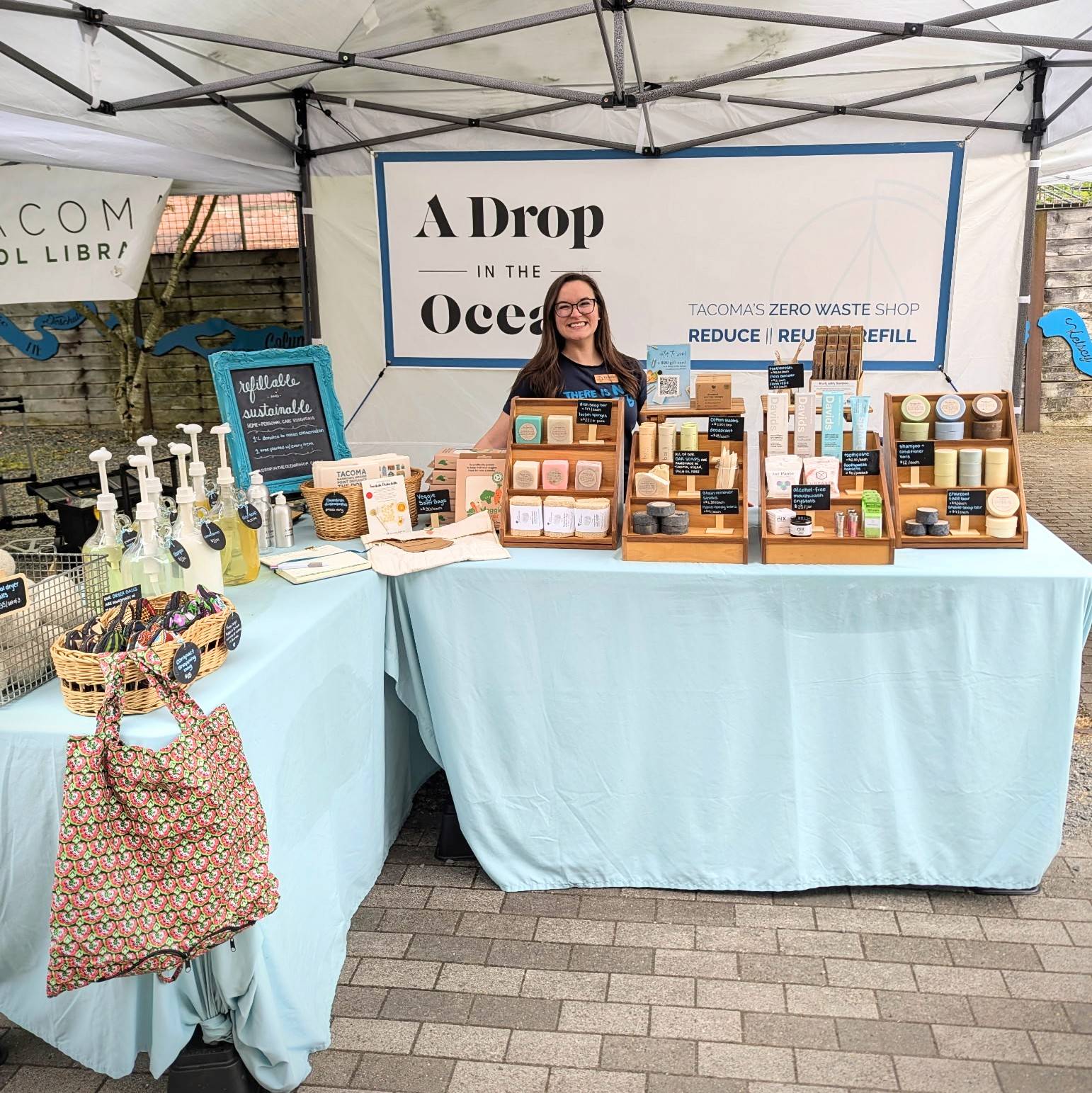 A Drop in the Ocean founder, Krystina, standing behind her booth at a local sustainability-focused market in Tacoma, WA