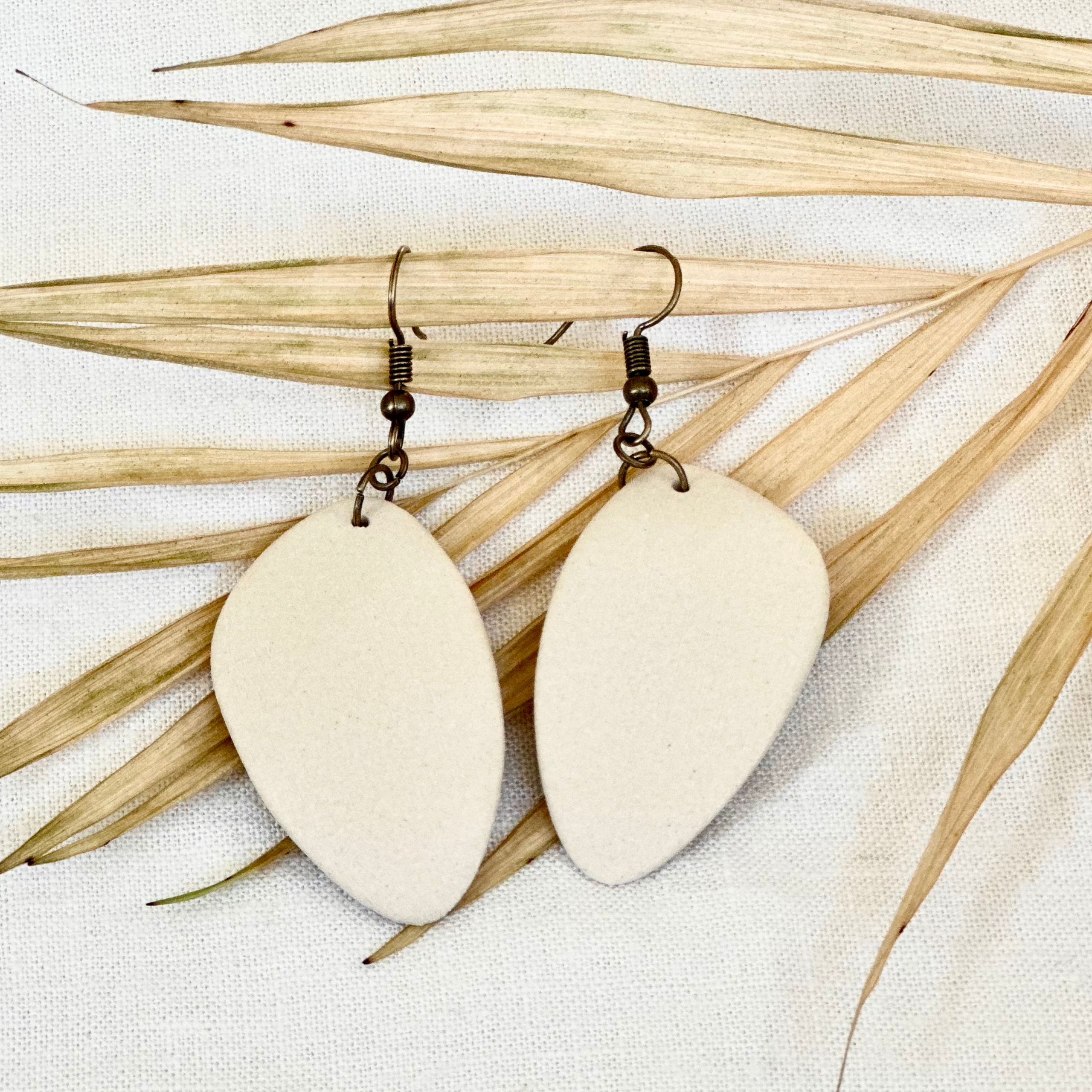 Off-white ceramic earrings being displayed over a tan dried leaf.