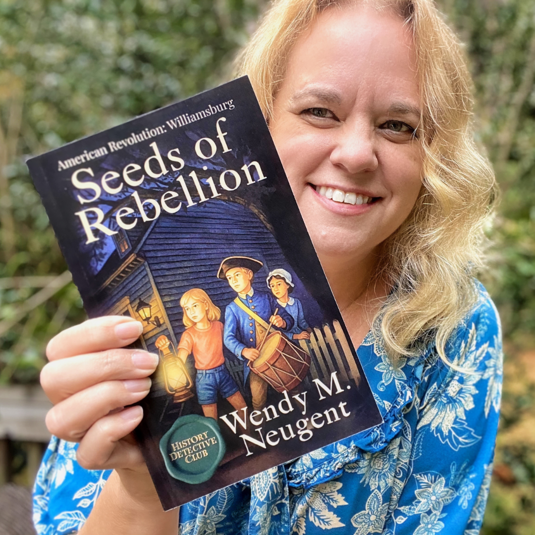 Author Wendy M. Neugent smiles while holding her book Seeds of Rebellion outdoors, with trees in the background.