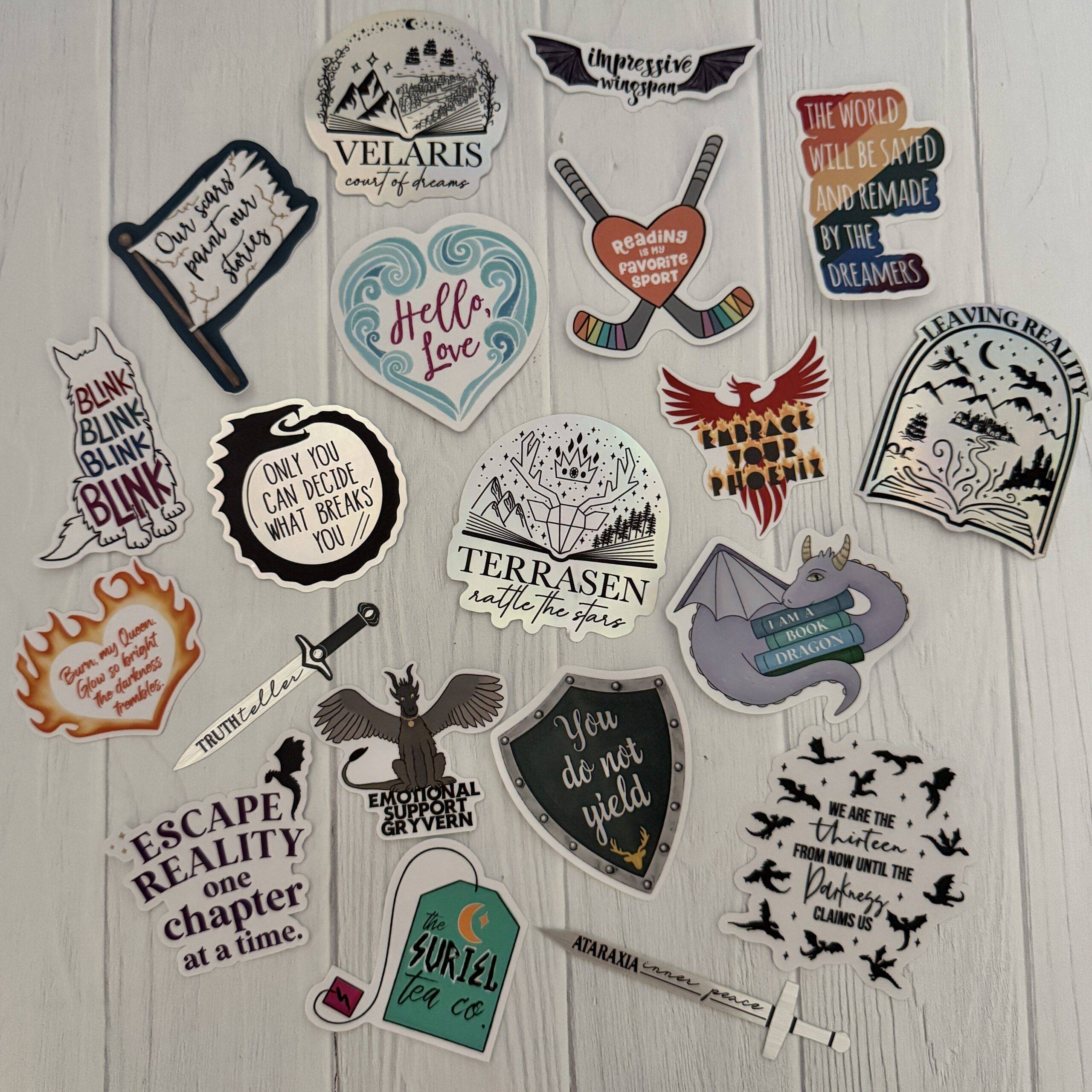 Flat lay of handmade bookish stickers from zoo&roo including designs from ACOTAR, Throne of Glass, Ever King, and Kindred’s Curse Saga on a white background.